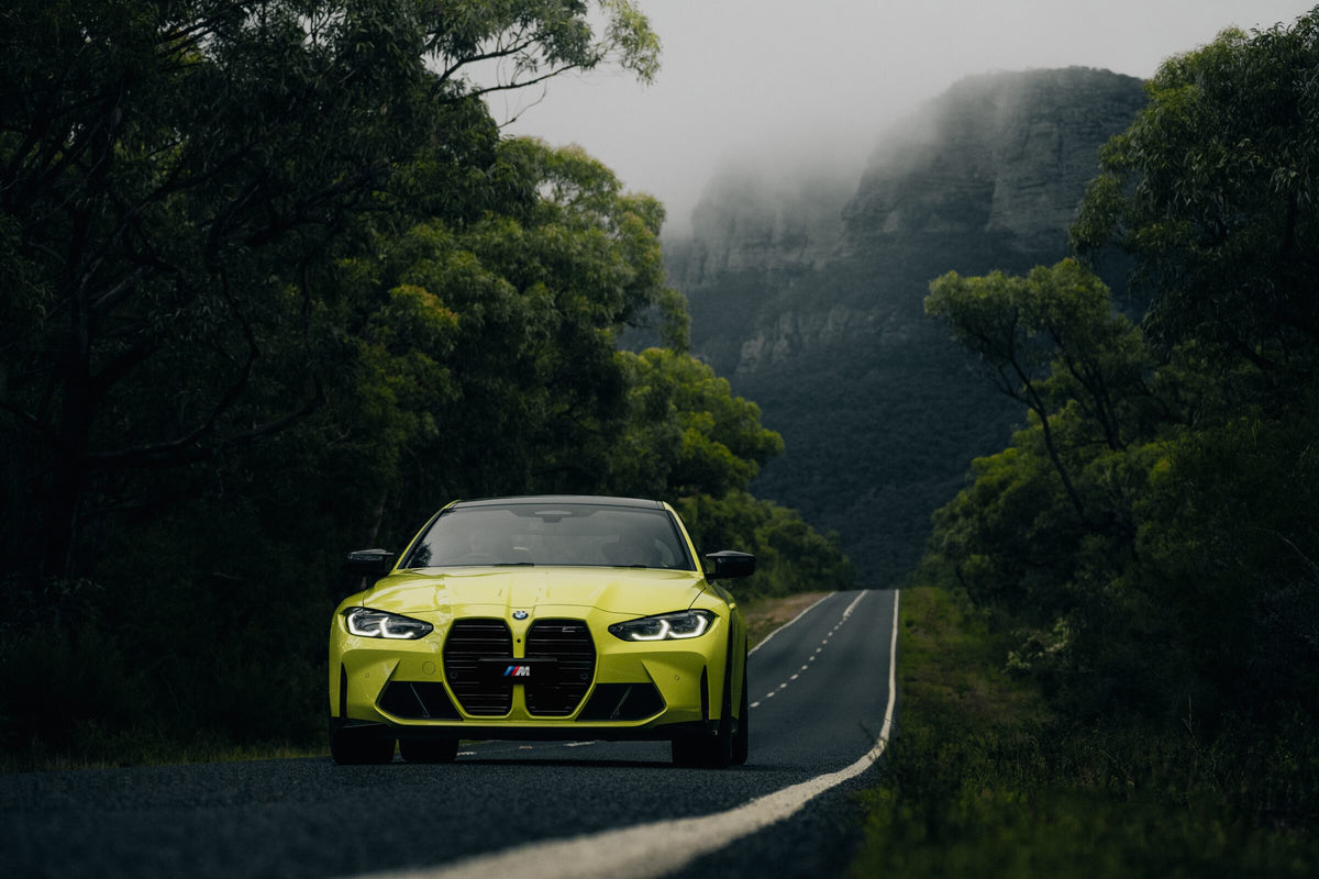 A BMW M4 head on, stopped on a road below misty Grampians cliffs