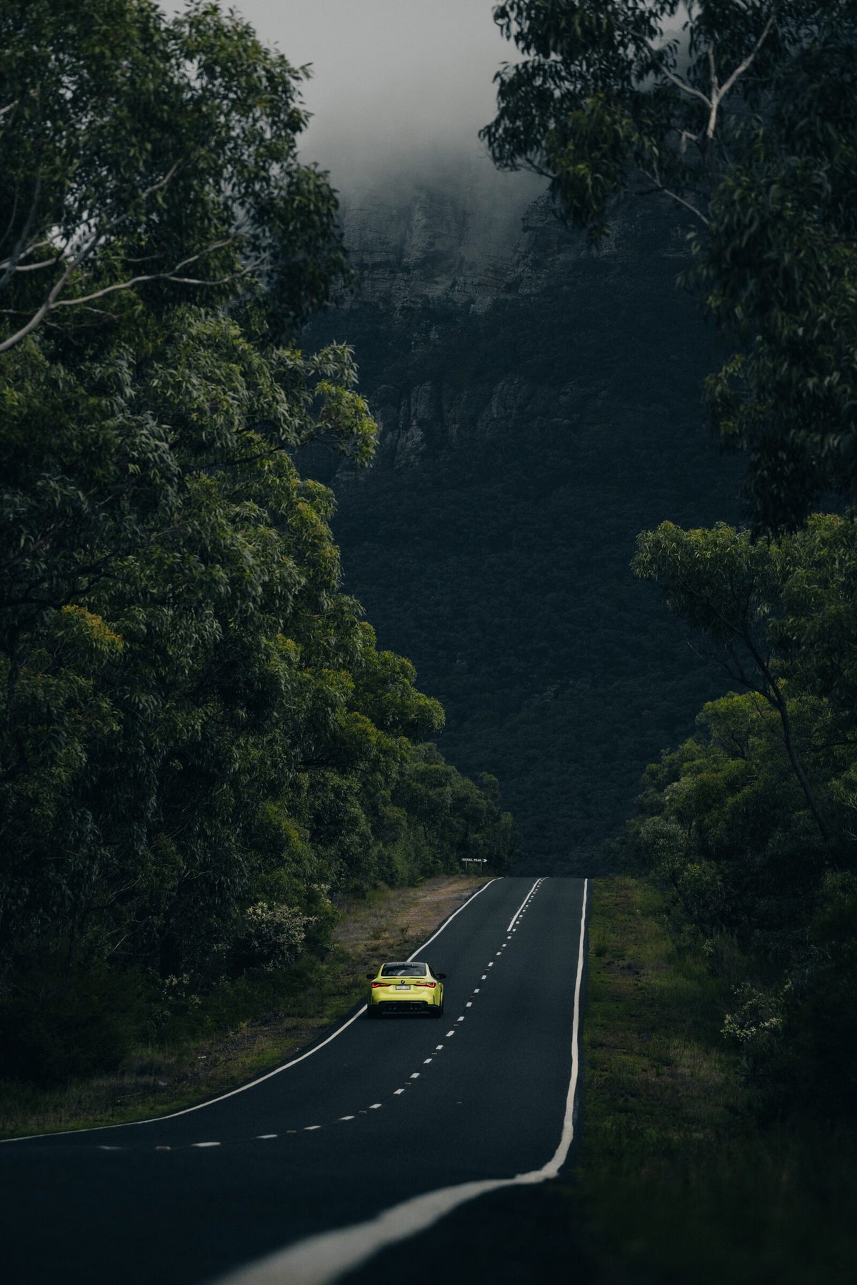 A BMW M4 driving away down an empty country road into the hills