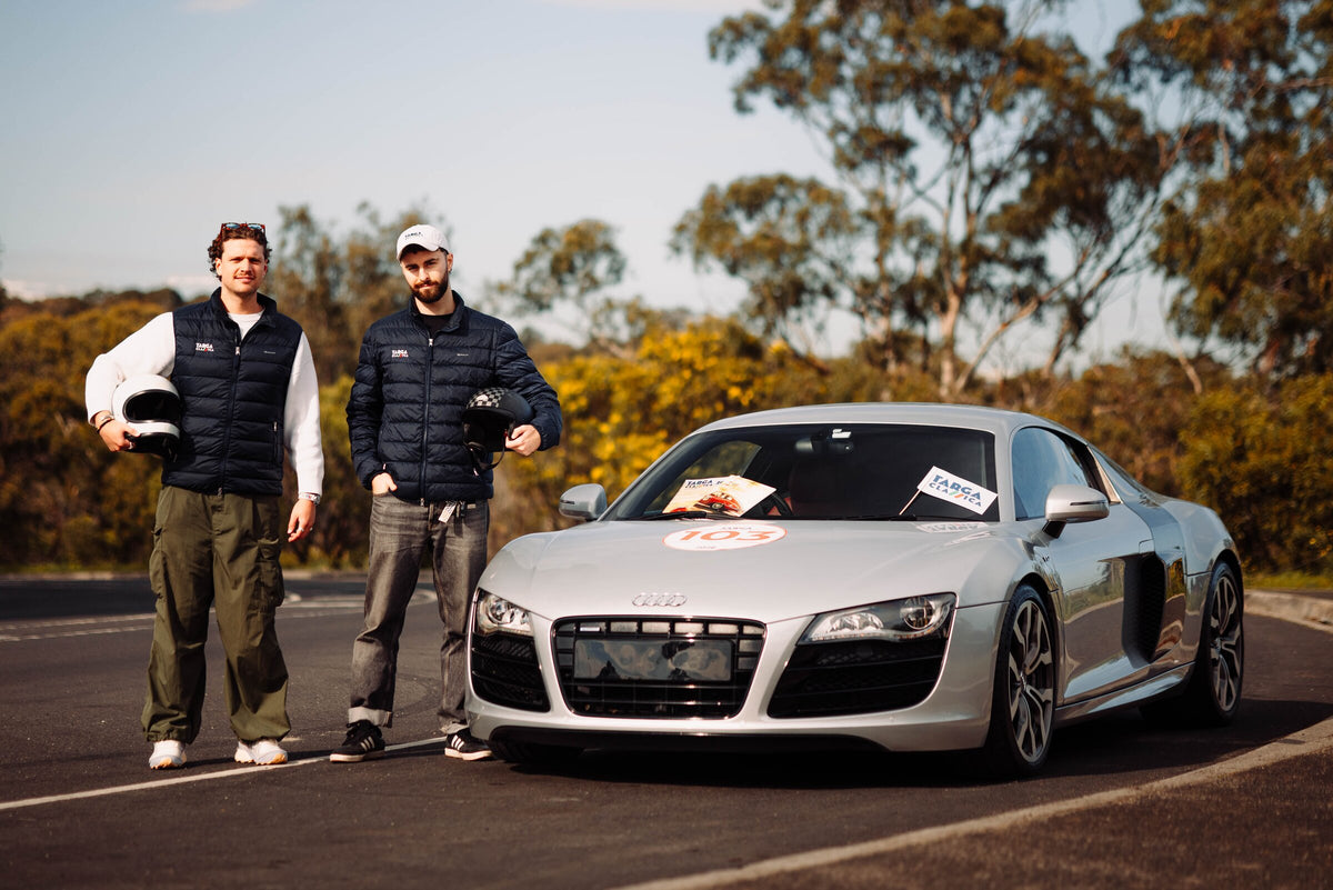 Two drivers holding helmets beside the car with its rally number